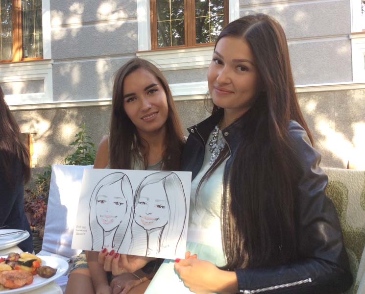 Две подруги позируют шаржисту за столом 